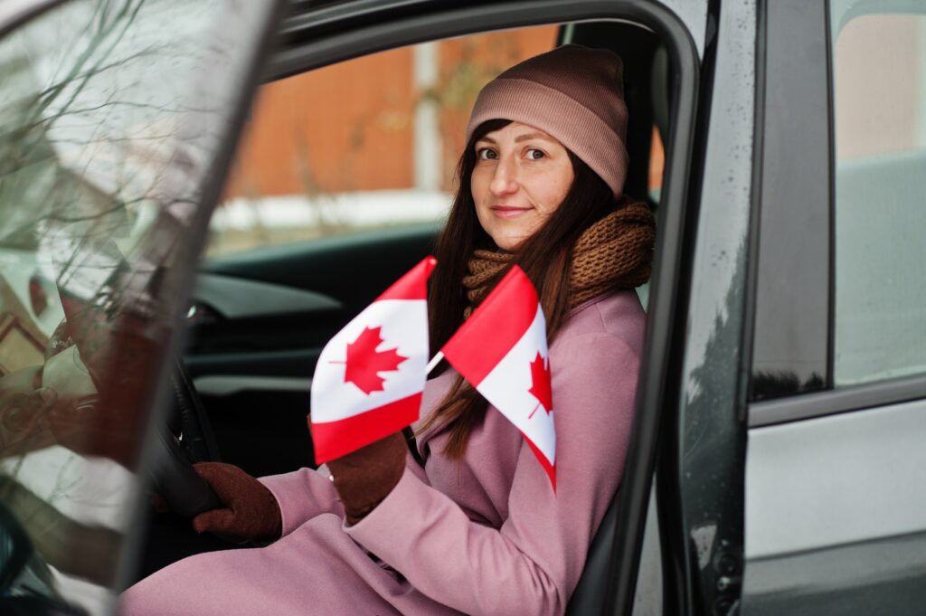 Young woman with Canada flag siting on car.
